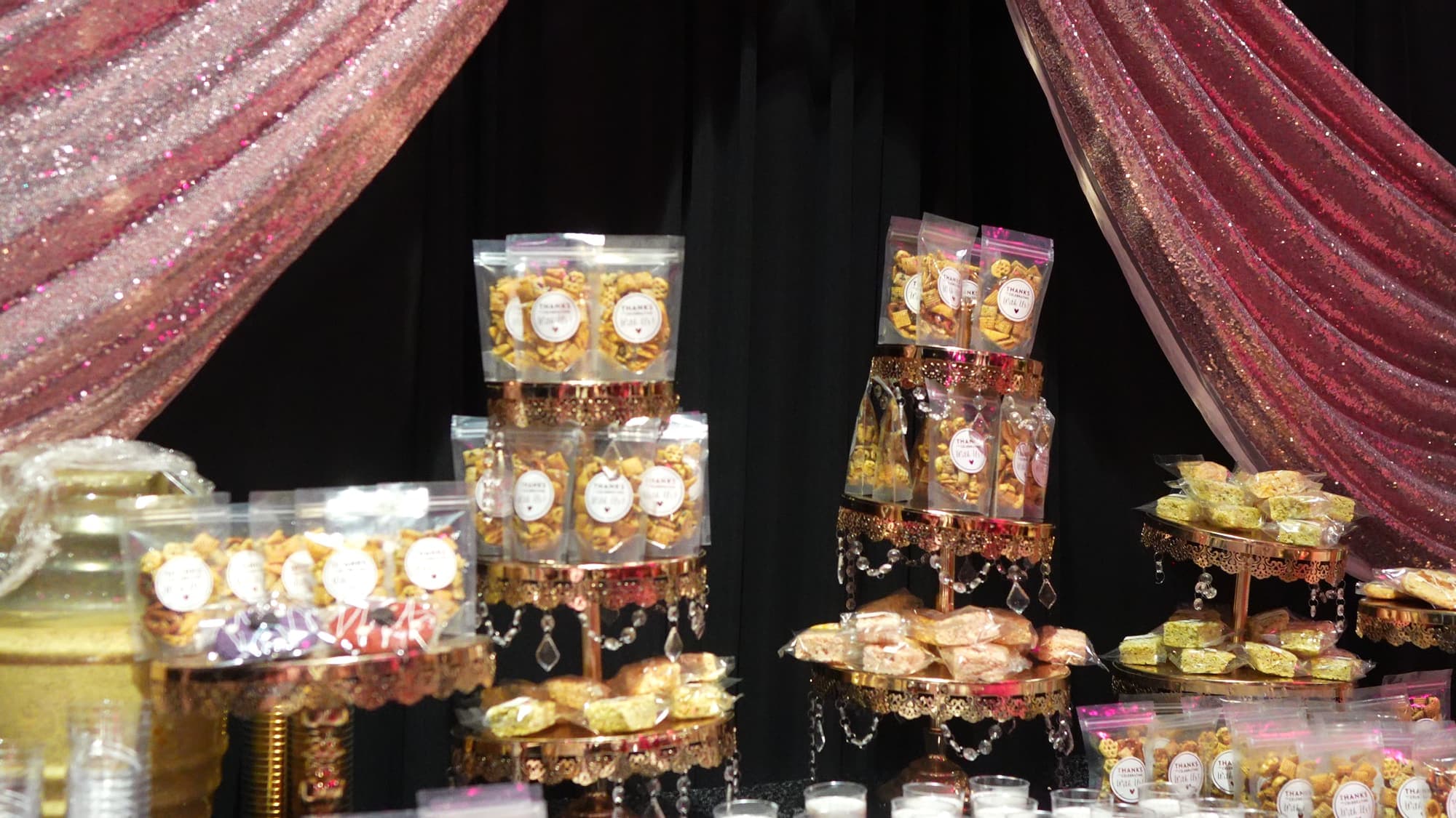 A dessert table of gold-wrapped treats under pink sequin drapes at an 18th birthday