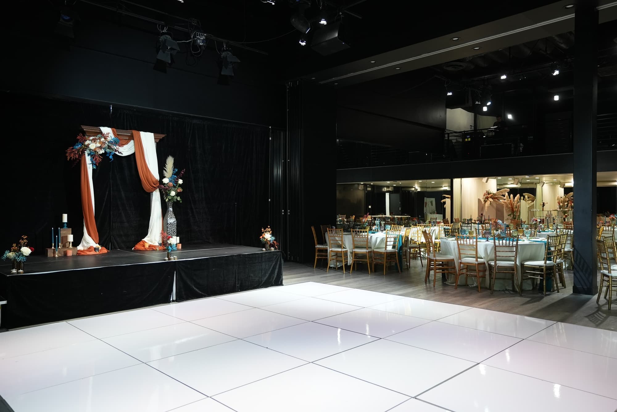 A draped floral arch on the stage behind a white dance floor